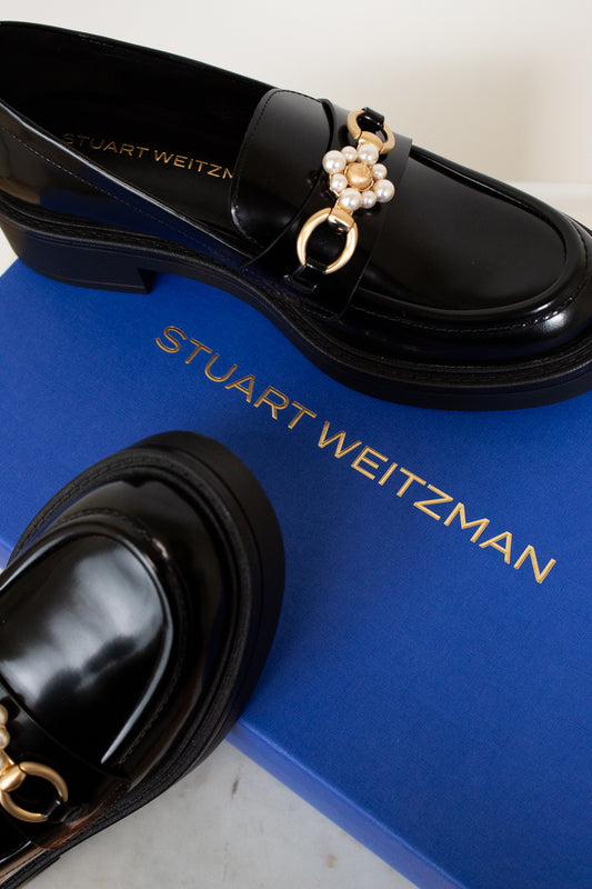 Black loafers with decorative charm on a blue Stuart Weitzman box.