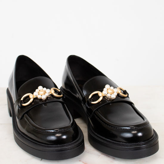 Black loafers with gold chain and pearl embellishments on a white background