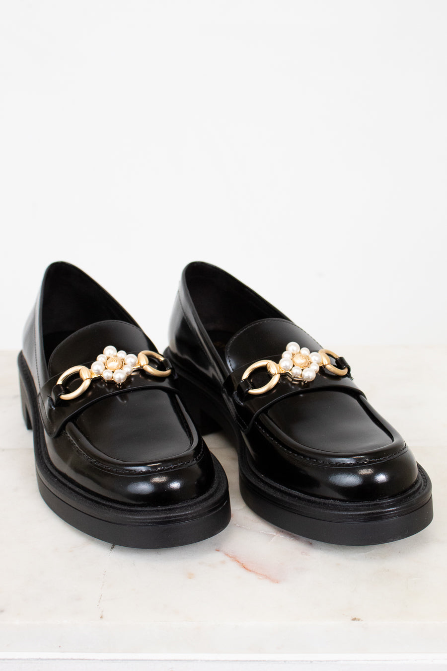 Black loafers with gold chain and pearl embellishments on a white background