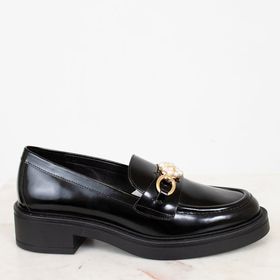 Black loafer shoe with a gold buckle on a white background