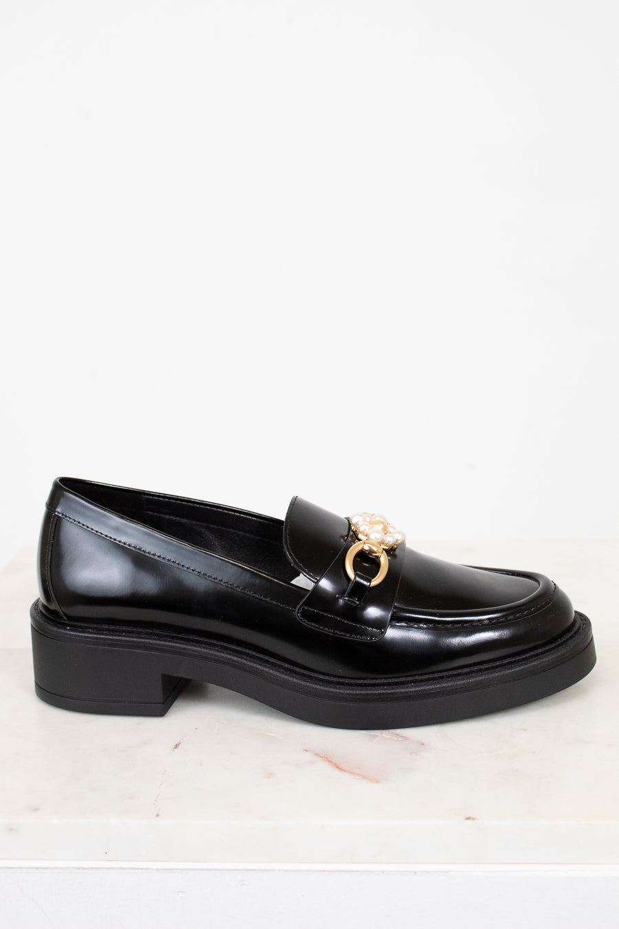 Black loafer shoe with a gold buckle on a white background