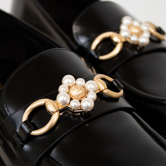 Black loafers with gold and pearl embellishments on a white background