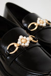 Black loafers with gold and pearl embellishments on a white background