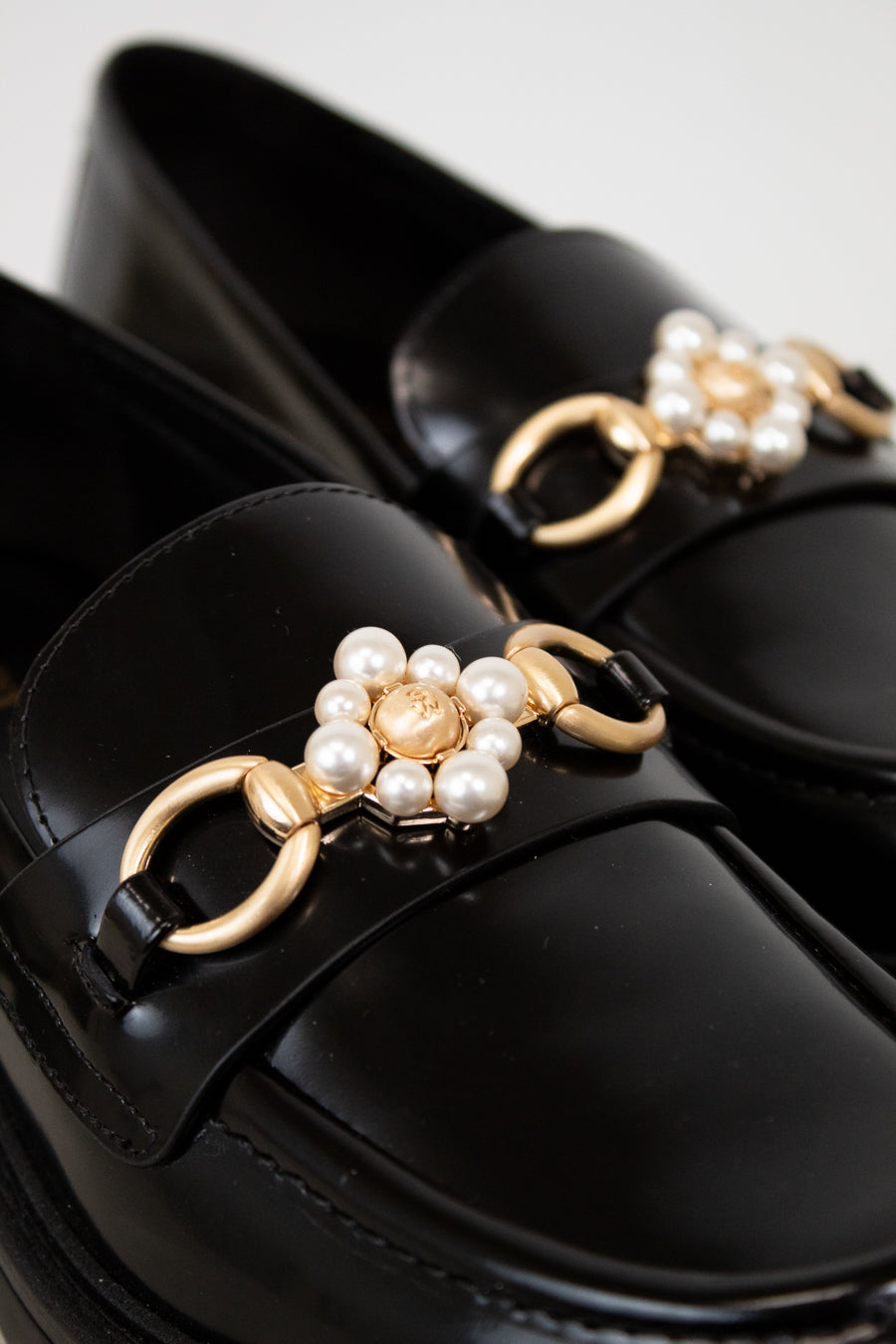 Black loafers with gold and pearl embellishments on a white background