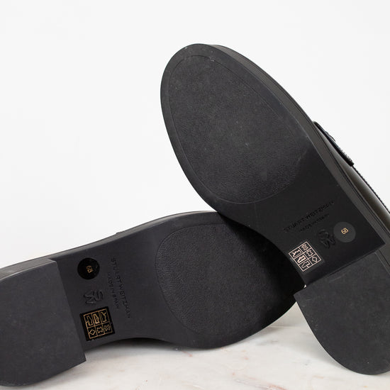 Close-up of black shoe soles with visible branding on a white background