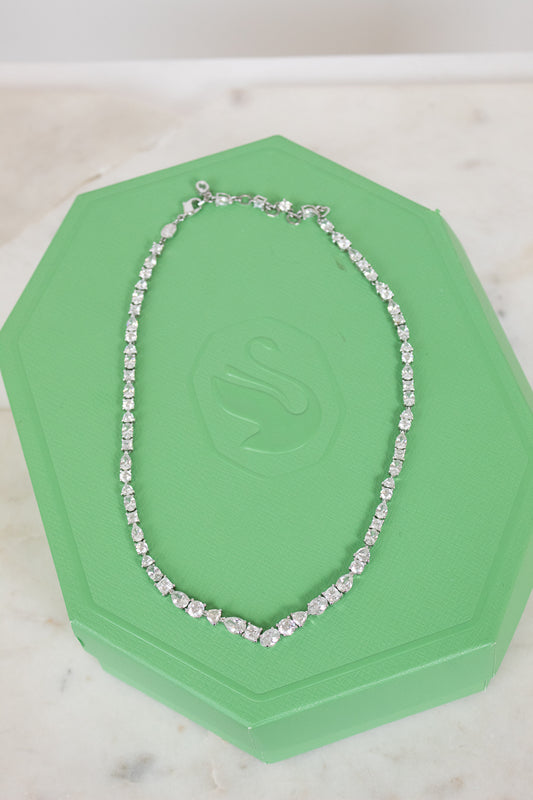 Crystal multi-sized tennis-like necklace laying on a green hexagonal box and against a plain marble surface