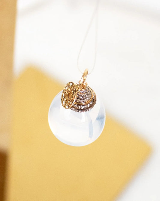 Gold and diamond pendant on a white string against a yellow background
