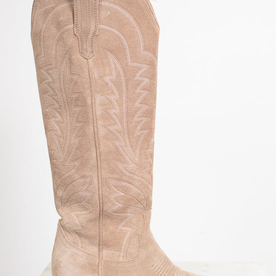 A single knee-high western boot in light tan suede with white embroidered stitching, shown in profile against a plain white background.