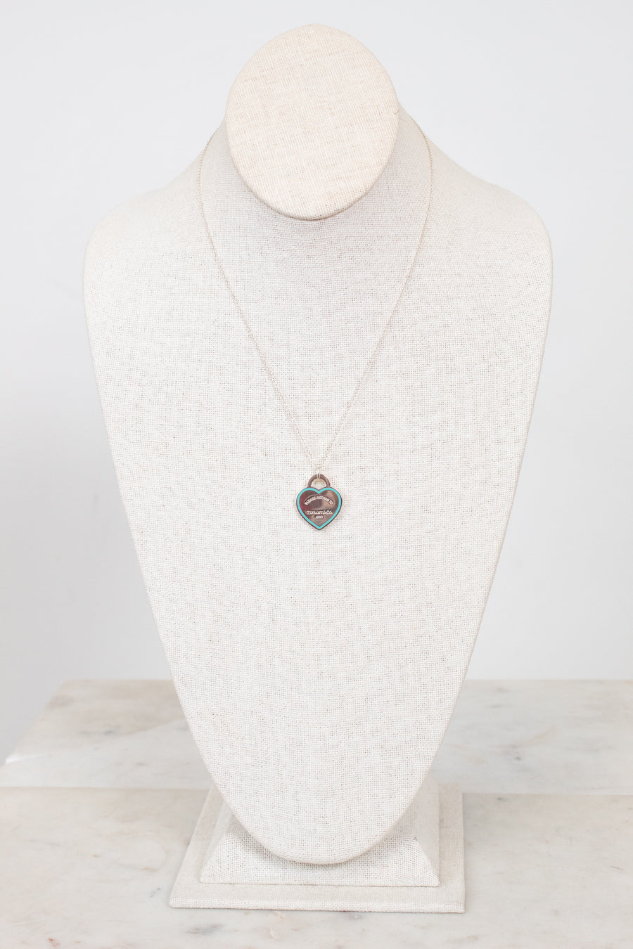 Dainty chain necklace with heart-shaped pendant on a white textured mannequin bust