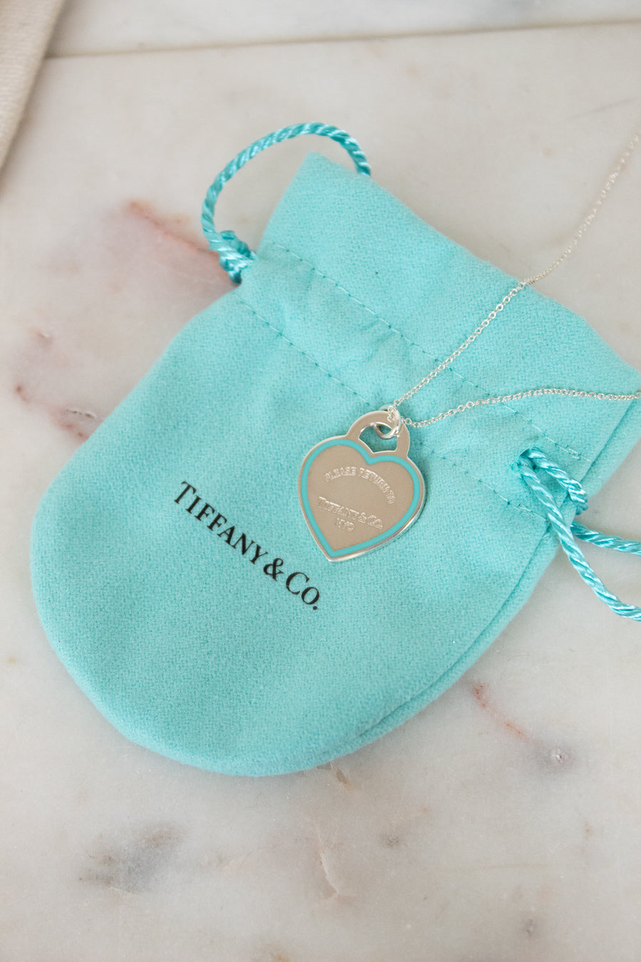 Tiffany & Co. necklace with heart tag on a turquoise pouch on a marble surface