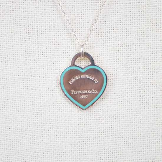 Heart-shaped tag pendant on a chain against a textured white background
