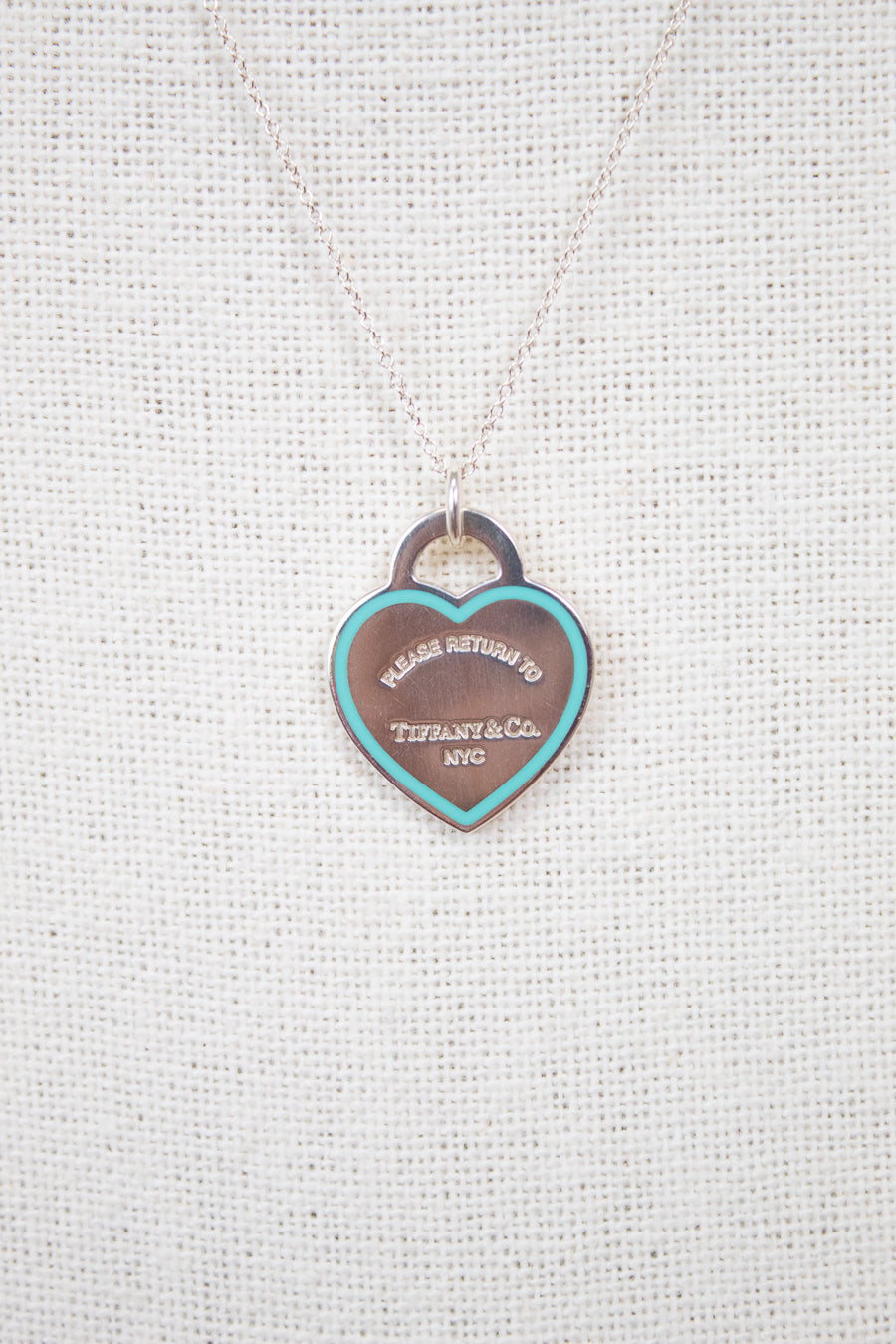 Heart-shaped tag pendant on a chain against a textured white background