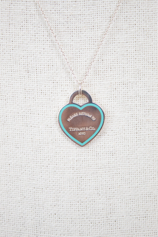 Heart-shaped tag pendant on a chain against a textured white background