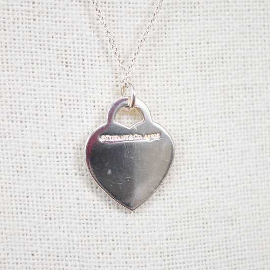 Back of heart-shaped pendant with logo stamp on textured white background