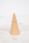 A thin silver band ring displayed on a light wood cone ring holder over a white marble surface.