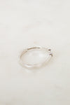 A silver open band ring with a small side accent, resting on a light beige marble surface. The inside of the band features a visible engraving reading 'Tiffany & Co.