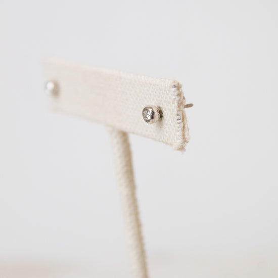 A side picture of TIFFANY & CO. silver diamond stud earrings placed on a beige earring holder and has a white background.