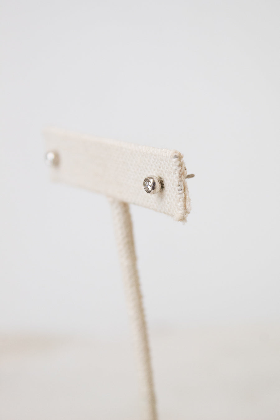 A side picture of TIFFANY & CO. silver diamond stud earrings placed on a beige earring holder and has a white background.