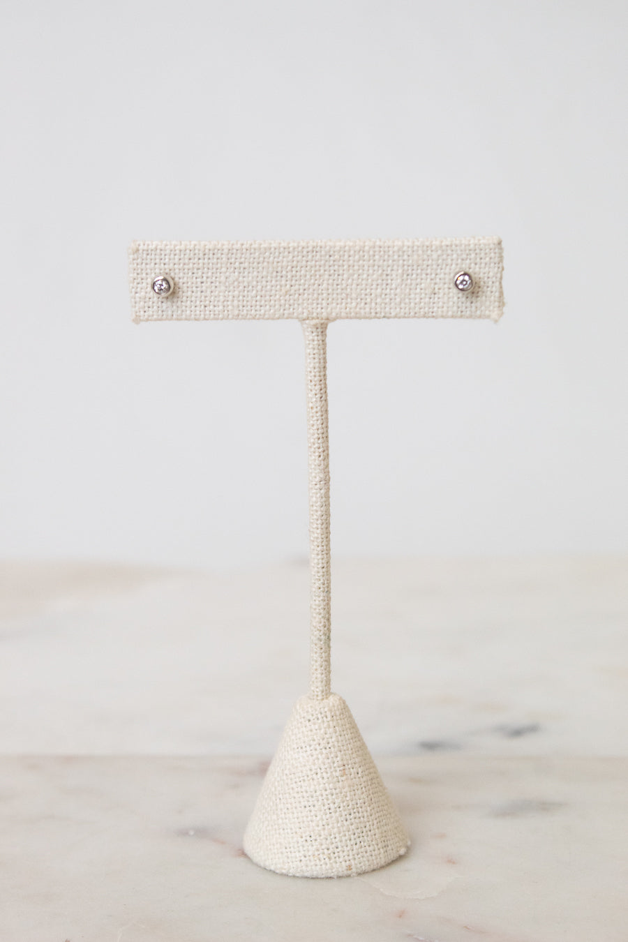 Front view of TIFFANY & CO. silver diamond circular stud earring resting on a beige earring stand , with a white and marble background.