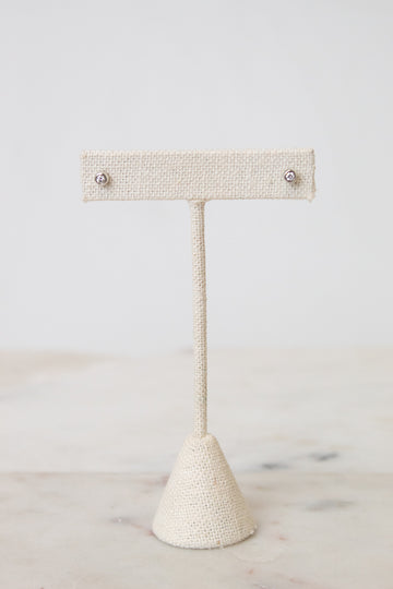 Front view of TIFFANY & CO. silver diamond circular stud earring resting on a beige earring stand , with a white and marble background.