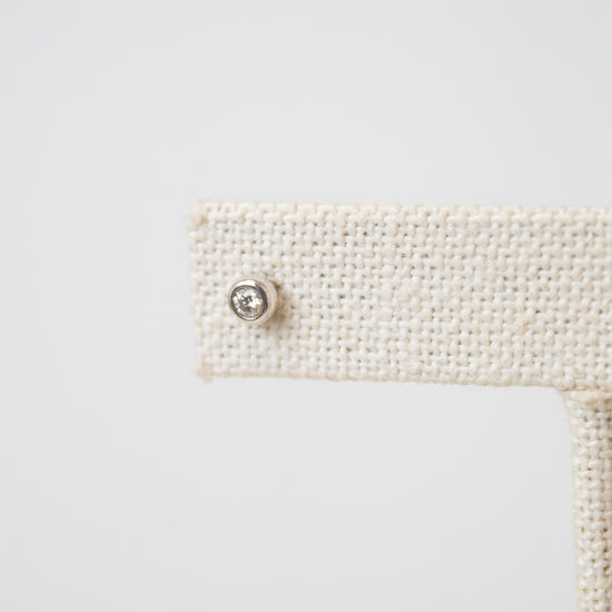 A close-up shot of one of the diamond studs, it is a circular shape with a diamond in the middle. The earring stud rest on a beige earring stand. 