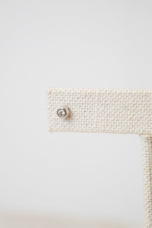 A close-up shot of one of the diamond studs, it is a circular shape with a diamond in the middle. The earring stud rest on a beige earring stand. 