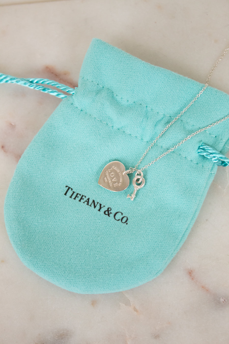 Tiffany & Co. necklace with heart and key charms on a turquoise pouch.