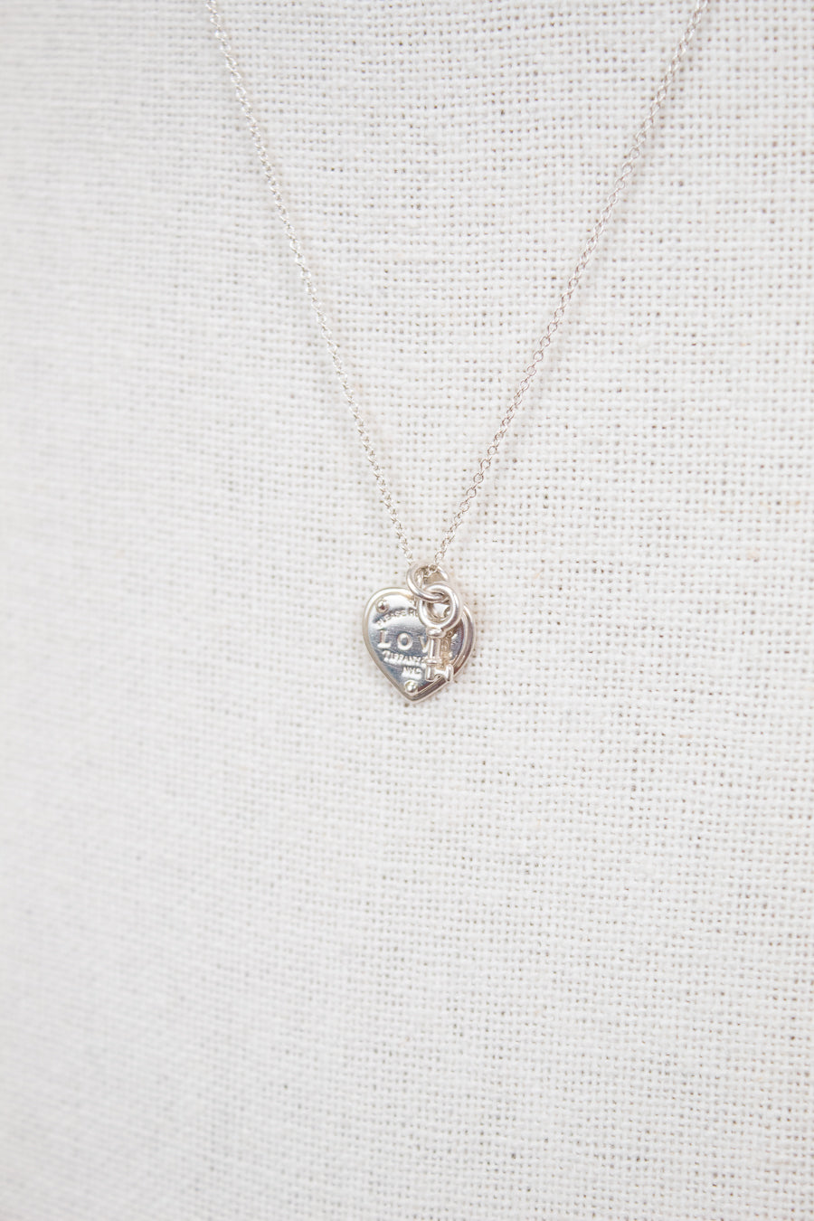 Silver heart-shaped pendant necklace on a light gray fabric background