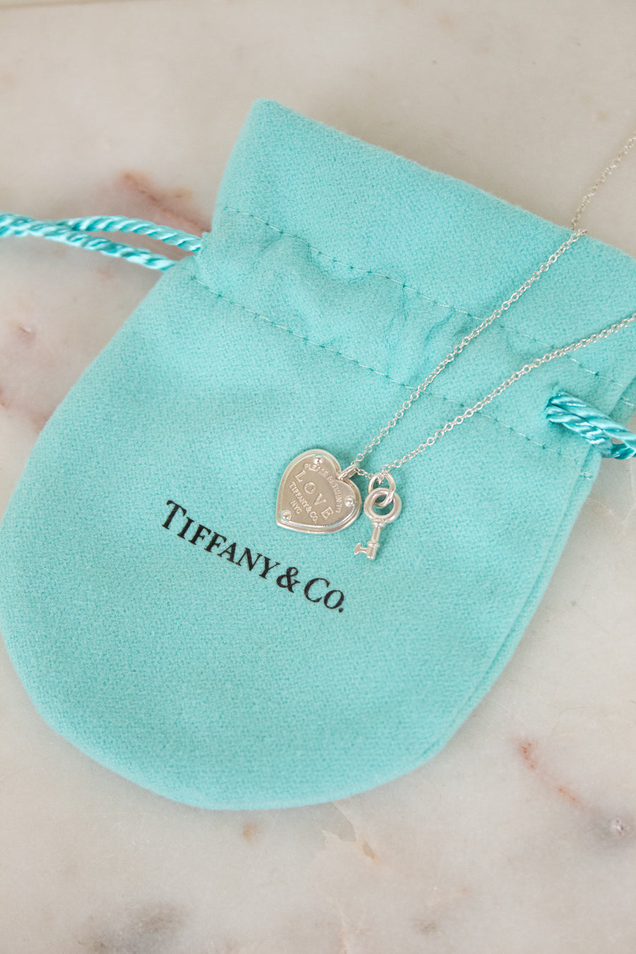 Tiffany & Co. necklace with heart and key charms on a turquoise pouch.
