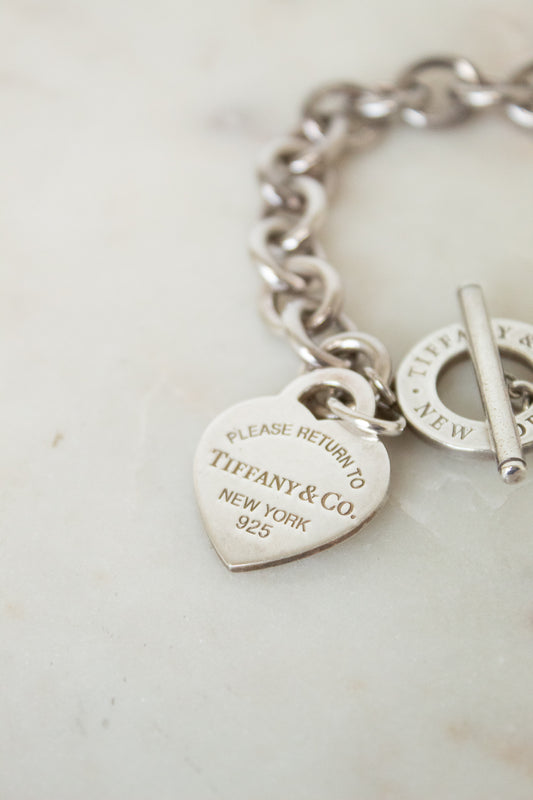 Close -Up of a silver Tiffany & Co. heart charm engraved " PLEASE RETURN TO TIFFANY & CO. NEW YORK 925"