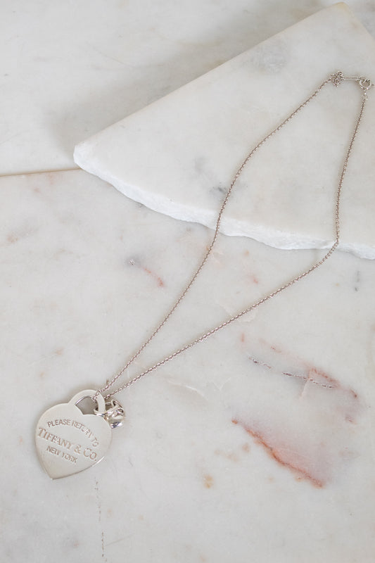 Silver necklace with heart-shaped pendant on a marble surface