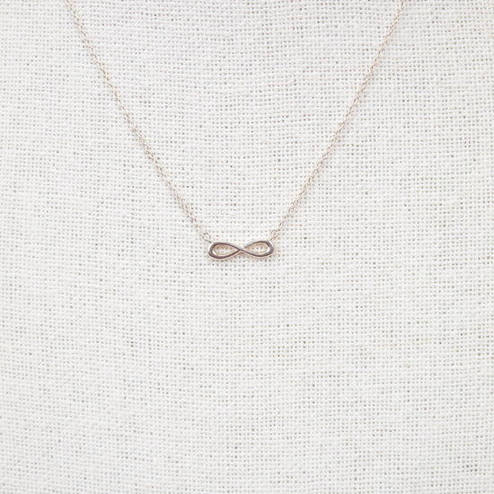 Silver infinity symbol necklace on a light gray textured background