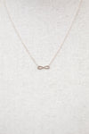 Silver infinity symbol necklace on a light gray textured background