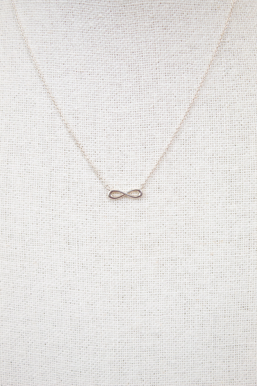 Silver infinity symbol necklace on a light gray textured background