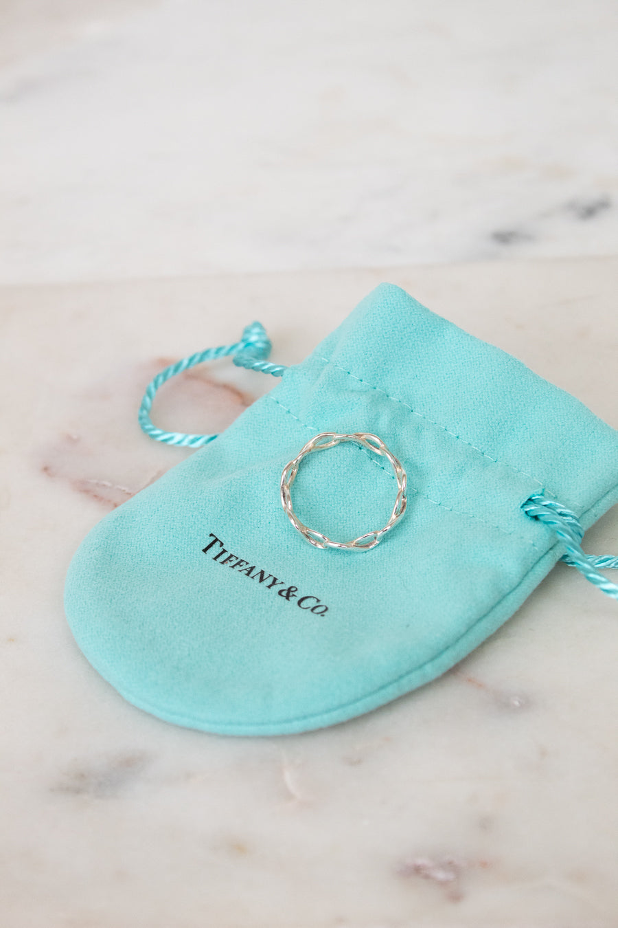 Silver ring on a Tiffany & Co. branded turquoise pouch on a marble surface