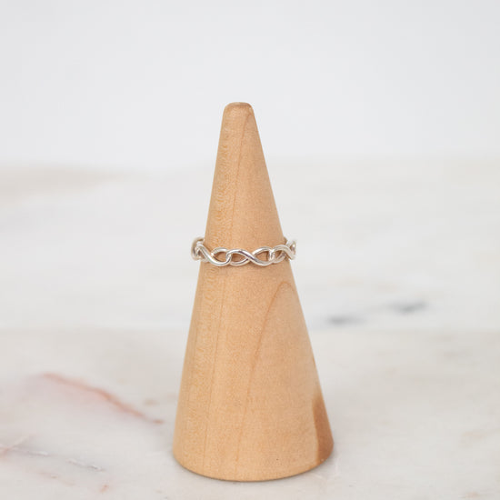 Silver ring on a wooden cone against a light background