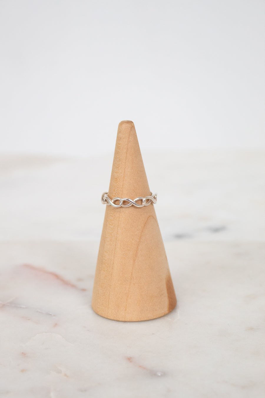 Silver ring on a wooden cone against a light background