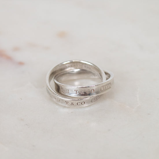 Two interlocking silver rings with engraved text on a marble surface