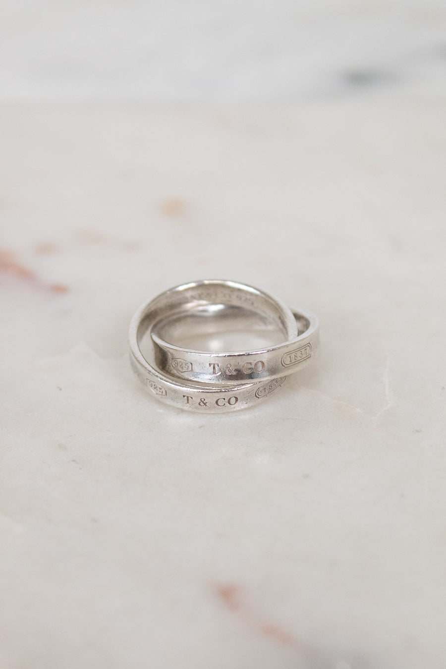 Two interlocking silver rings with engraved text on a marble surface