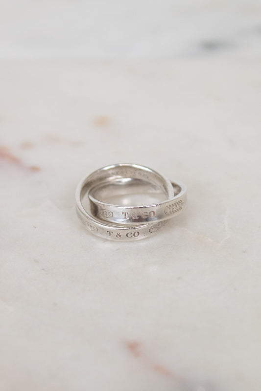 Two interlocking silver rings with engraved text on a marble surface
