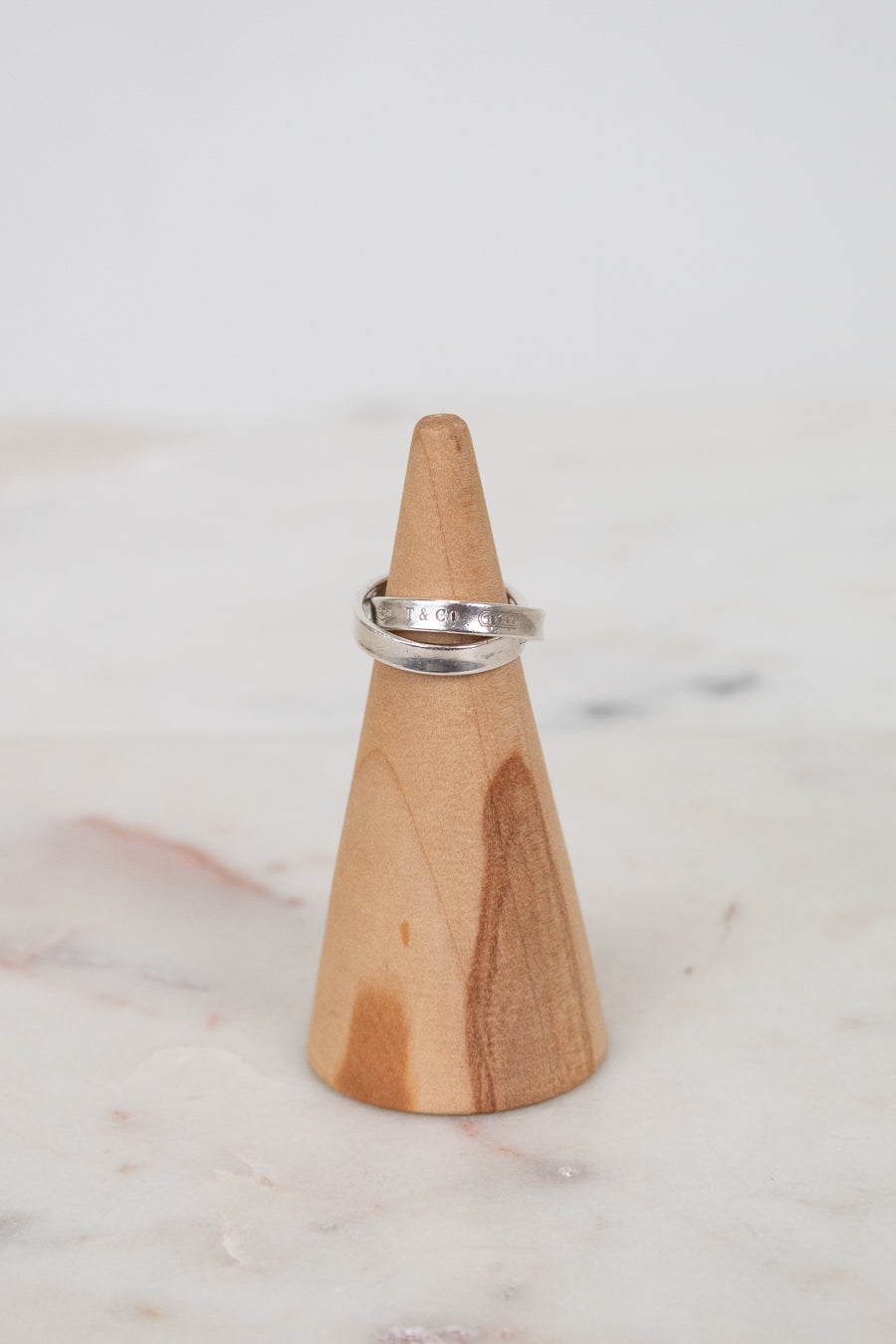Silver ring on a wooden ring stand against a marble background