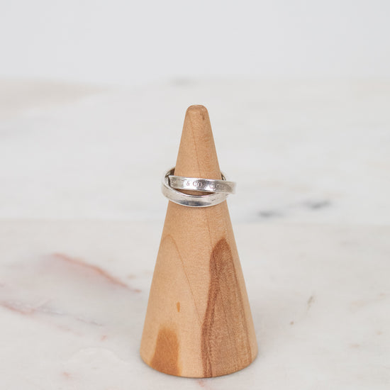 Wooden cone-shaped ring holder with a silver ring on a marble surface