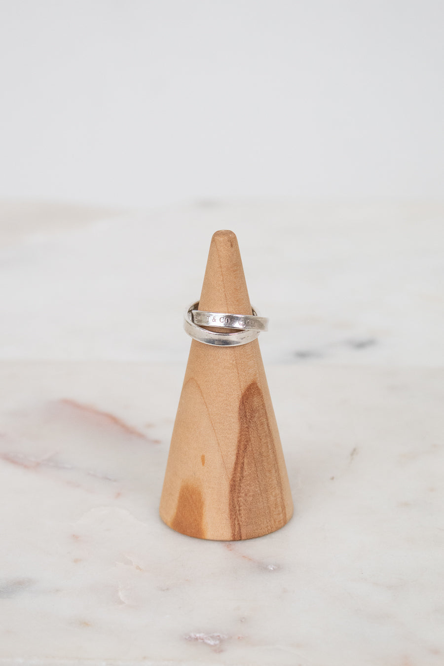 Wooden cone-shaped ring holder with a silver ring on a marble surface