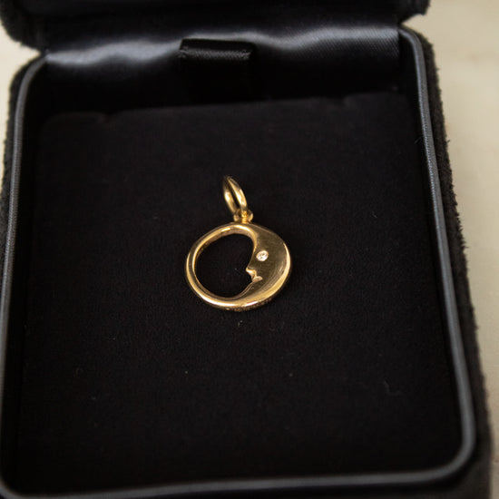 Gold pendant with moon and face design in a black jewelry box
