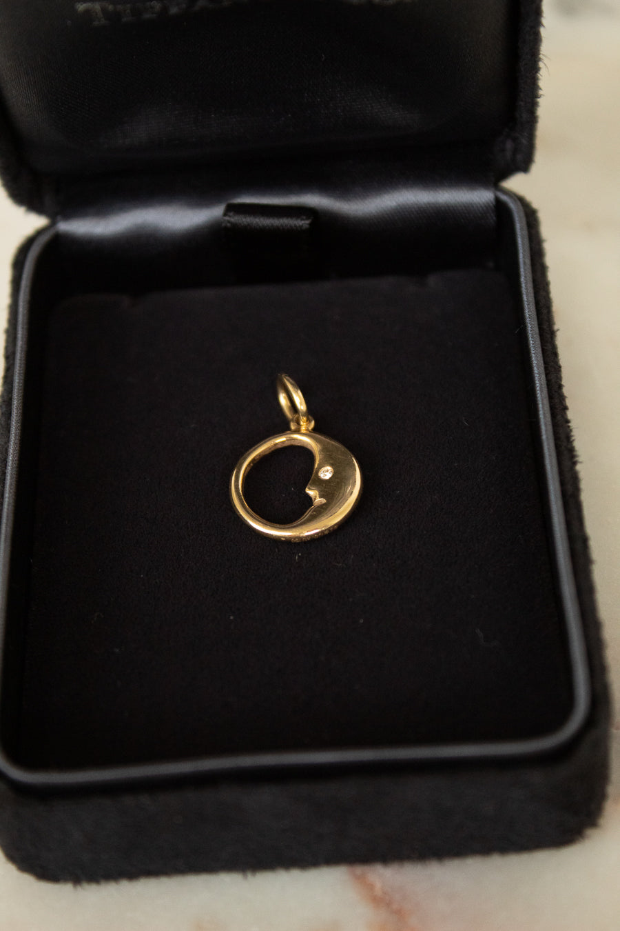 Gold pendant with moon and face design in a black jewelry box