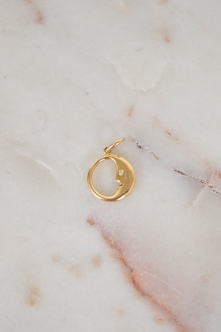 Gold pendant with a small diamond on a marble surface