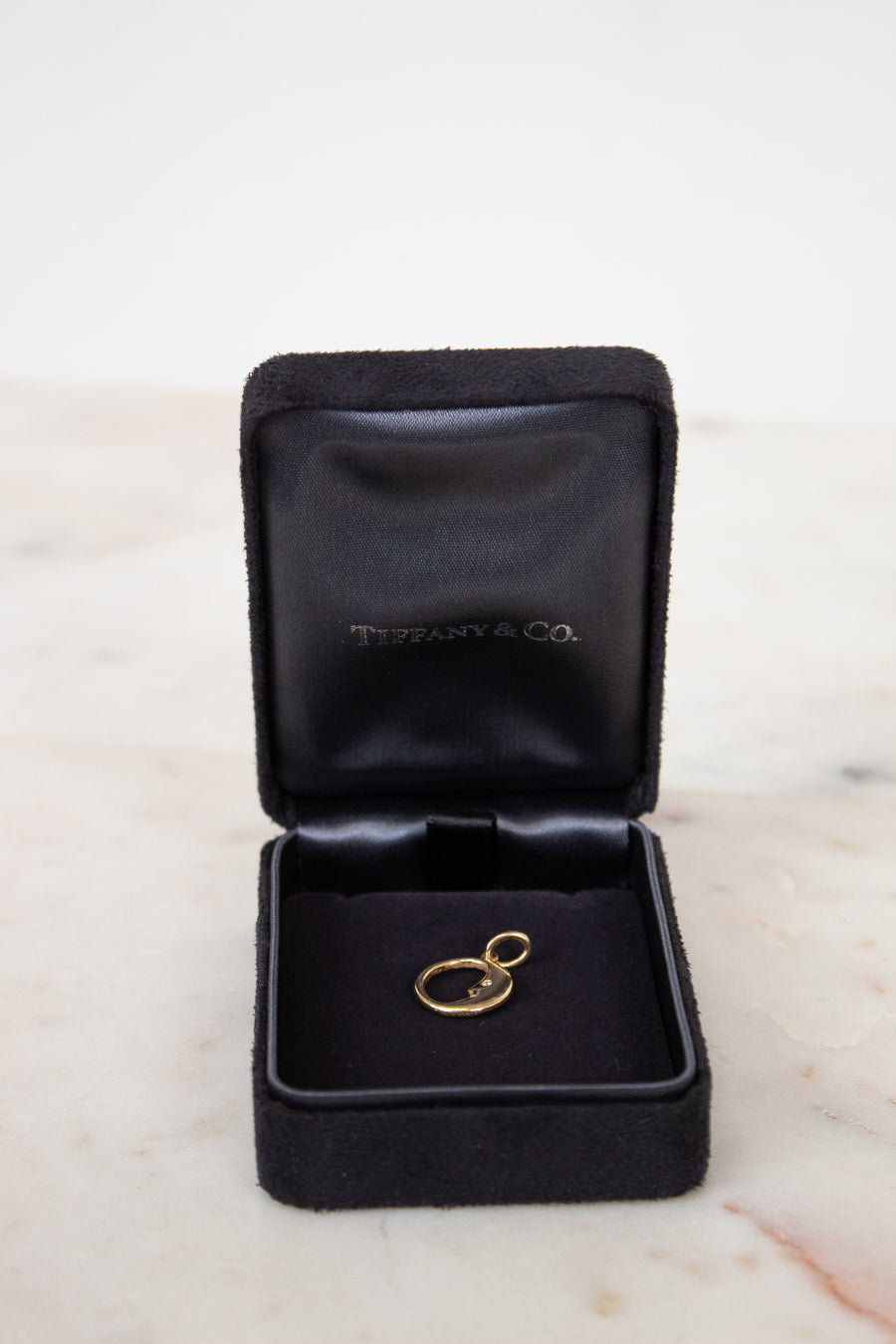 Gold pendant in a black Tiffany & Co. jewelry box on a marble surface