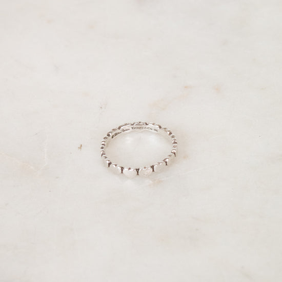 A delicate silver beaded ring resting on a light beige marble surface.