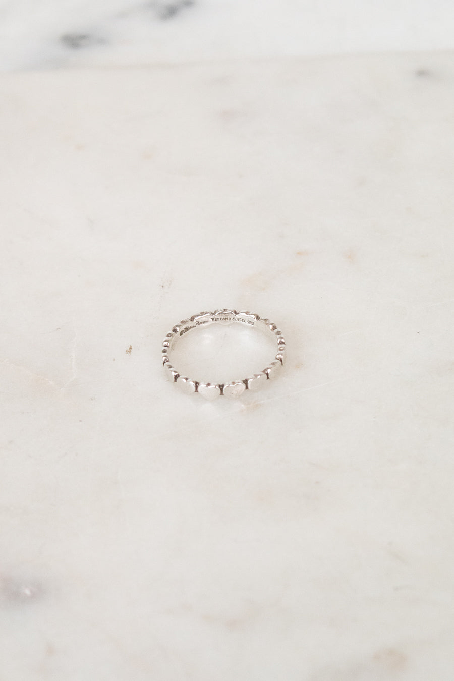 A delicate silver beaded ring resting on a light beige marble surface.
