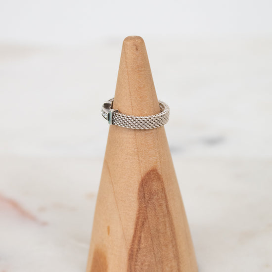 Wooden cone-shaped ring holder with a silver ring on a white background